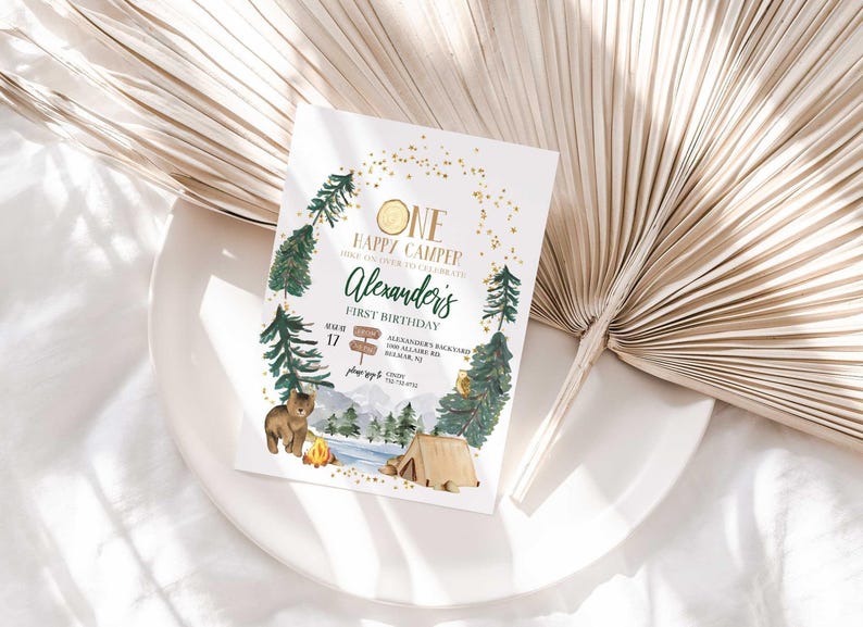 Lifestyle photo of Alexander's camping-themed birthday invitation propped on a white plate with a dried palm frond, styled on a linen tablecloth.