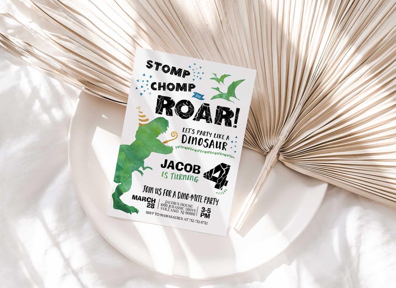 Jacob's dinosaur-themed birthday invitation displayed on a white plate with a dried palm frond, on a white linen background.