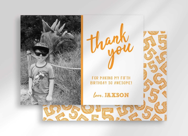 Styled mockup of a photo thank you card front layered over its gold number-5 patterned card back. Front shows a black-and-white photo insert of a boy wearing sunglasses and a cap at a dinosaur exhibit, beside orange "thank you" text reading "for making my fifth birthday so awesome! love, Jaxson."