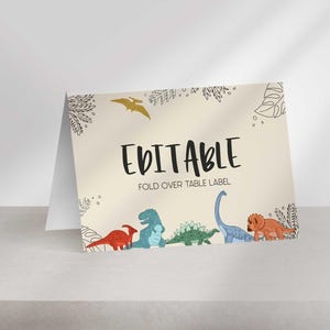 A folded tent card sits on a light surface with dinosaur illustrations and the text EDITABLE FOLD OVER TABLE LABEL.