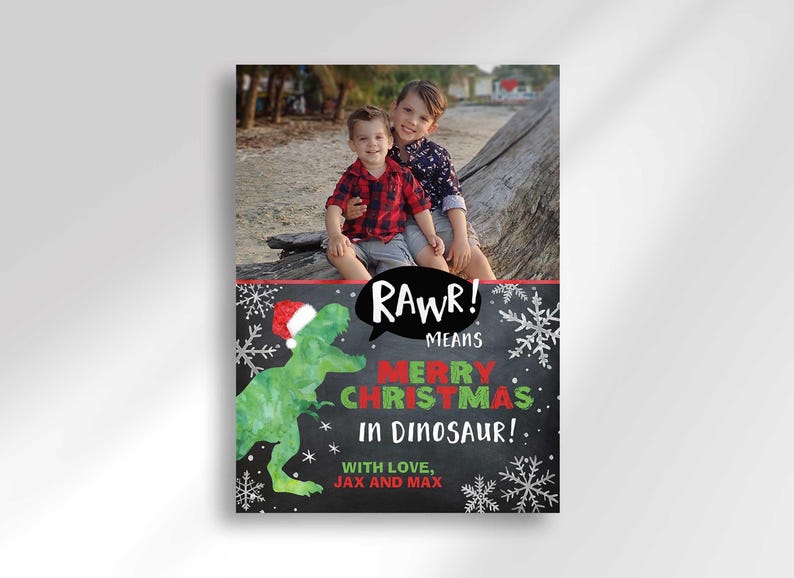 A vertical Christmas card with a photo of two boys on a beach and a green dinosaur wearing a Santa hat.