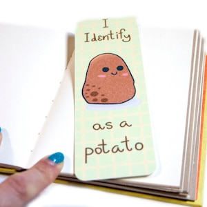 May include: A green and white bookmark with a cartoon potato with a smiling face. The bookmark says "I Identify as a potato".
