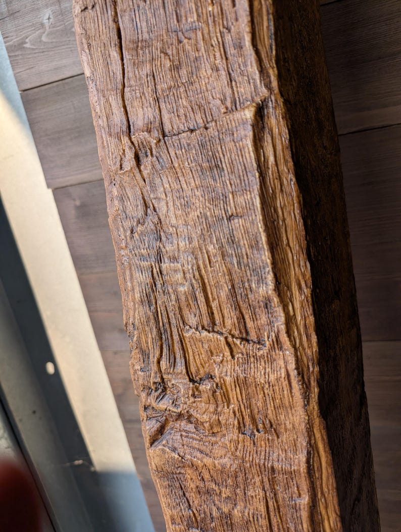 May include: A rectangular wooden beam featuring a deep, textured grain pattern with a medium brown finish. The surface displays prominent vertical ridges, natural cracks, and a weathered appearance across its elongated, solid structural form.