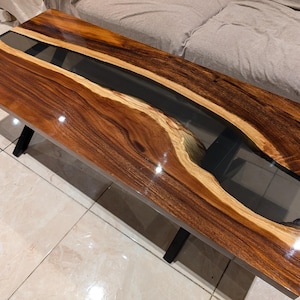 May include: A dark wood coffee table with a black epoxy river running through the center. The table has a glossy finish and is supported by a black metal X-shaped base.