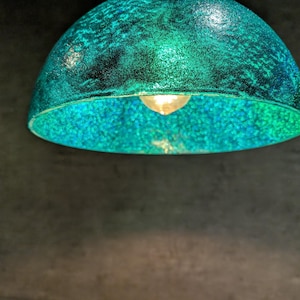 May include: A teal blue, round, textured lampshade with a light bulb inside.