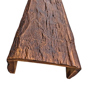 Può includere: Una trave architettonica a forma di U con una finitura marrone scuro e una superficie profondamente strutturata che imita l'aspetto del legno stagionato e grezzo. La trave presenta venature, creste e scanalature prominenti sull'esterno.