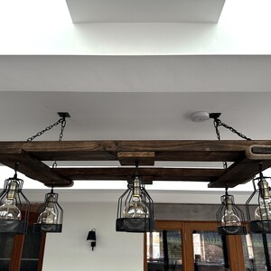 May include: A rustic wooden chandelier with five black caged light fixtures hanging from a reclaimed wood frame. The chandelier is suspended from the ceiling with black chains.