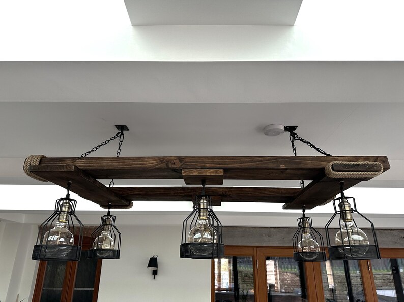 May include: A rustic wooden chandelier with five black caged light fixtures hanging from a reclaimed wood frame. The chandelier is suspended from the ceiling with black chains.