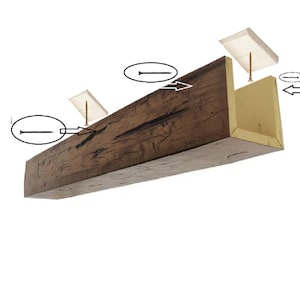 May include: A hollow U-shaped wooden beam with a dark brown, textured exterior and a light tan interior. The beam is shown with two white mounting blocks, two long screws, and two smaller screws, with arrows indicating the installation process.