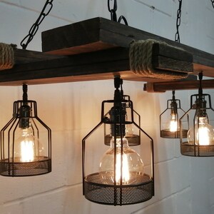 May include: A rustic wooden chandelier with six caged light bulbs. The chandelier is made of reclaimed wood and has a rope detail. The light bulbs are Edison style and have a warm glow.