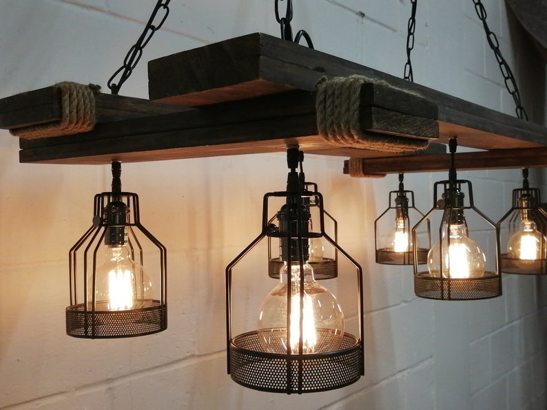 May include: A rustic wooden chandelier with six caged light bulbs. The chandelier is made of reclaimed wood and has a rope detail. The light bulbs are Edison style and have a warm glow.
