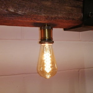May include: A single light bulb hanging from a wooden beam. The bulb is a clear glass teardrop shape with a warm white light. The bulb is attached to a brass socket.