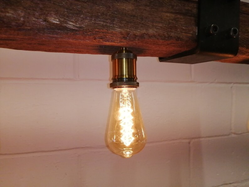May include: A single light bulb hanging from a wooden beam. The bulb is a clear glass teardrop shape with a warm white light. The bulb is attached to a brass socket.