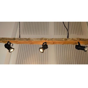 May include: A rustic wooden ceiling light fixture with three black spotlights. The wood is a natural, light brown colour with a rough, unfinished texture.