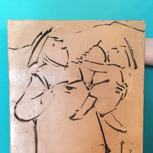 May include: A rectangular, tan-colored relief sculpture depicting a stylized mother and child. The figures are outlined in black, with the child held in the mother's arms. The artwork has a textured surface and a minimalist aesthetic.