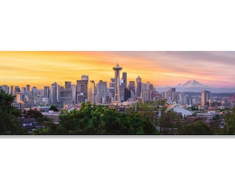May include: A panoramic view of the Seattle skyline at sunset, with the Space Needle and Mount Rainier in the distance. The city is bathed in warm, golden light, with a few clouds in the sky. The foreground is filled with lush green trees.