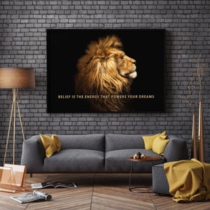 Pode incluir: Uma impress&atilde;o em tela emoldurada em preto com uma cita&ccedil;&atilde;o motivacional, "BELIEF IS THE ENERGY THAT POWERS YOUR DREAMS." A impress&atilde;o apresenta um close-up de uma cabe&ccedil;a de le&atilde;o com uma juba dourada sobre um fundo preto.