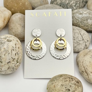 May include: Silver and gold earrings with a hammered texture and three concentric circles. The earrings are displayed on a white card with the word "SCAFATI" printed in gold.