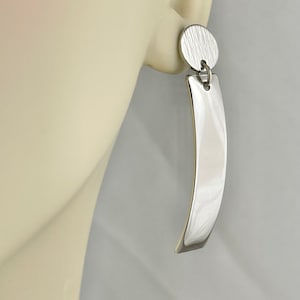 May include: Silver dangle earrings with a textured round disc and a long, curved rectangular pendant.