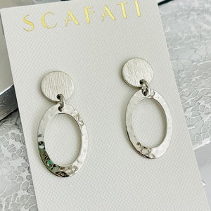 May include: Silver hammered circle earrings with a smaller hammered circle on top. The earrings are on a white card with the word "SCAFATI" printed in gold.