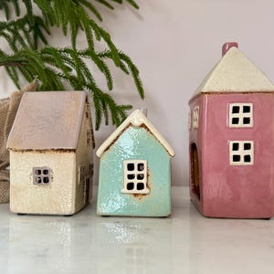 Peut inclure: Trois figurines de maison en c&eacute;ramique cr&egrave;me, turquoise et rose. Chaque maison a un toit contrastant et des fen&ecirc;tres carr&eacute;es. Les maisons sont d&eacute;coratives et conviennent &agrave; la d&eacute;coration int&eacute;rieure.