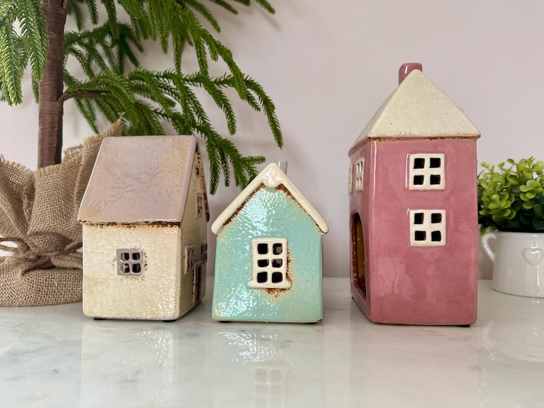 Peut inclure: Trois figurines de maison en c&eacute;ramique cr&egrave;me, turquoise et rose. Chaque maison a un toit contrastant et des fen&ecirc;tres carr&eacute;es. Les maisons sont d&eacute;coratives et conviennent &agrave; la d&eacute;coration int&eacute;rieure.