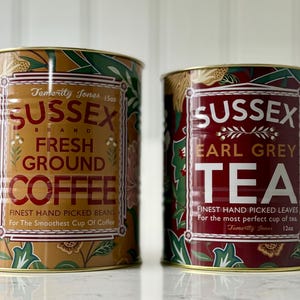 May include: Two decorative metal tins of Sussex Brand coffee and tea. The coffee tin is tan with red text and floral accents. The tea tin is red with white text and floral accents. Both tins have gold rims and are labeled with the brand name and product type.
