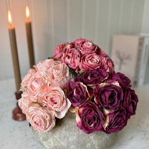 Könnte beinhalten: Ein Strauß aus rosa und burgunderfarbenen Rosen in einer grauen Betonvase. Die Rosen sind kreisförmig angeordnet und in voller Blüte.