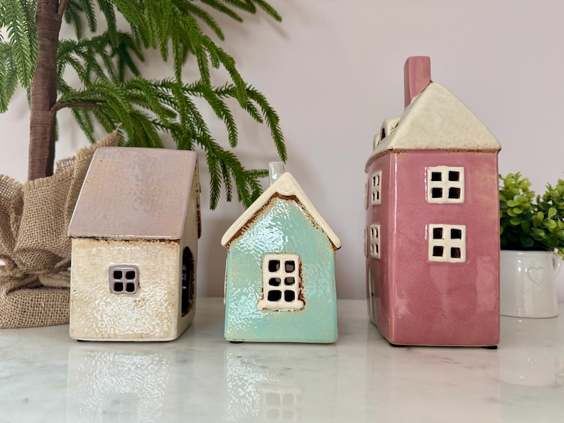 Peut inclure: Trois figurines de maisons en c&eacute;ramique aux couleurs pastel. Les maisons ont des fen&ecirc;tres carr&eacute;es et des toits de formes diff&eacute;rentes. Une est rose clair, une est bleu clair et une est blanc cass&eacute; avec un toit marron clair. D&eacute;coratives, elles conviennent &agrave; la d&eacute;coration int&eacute;rieure.