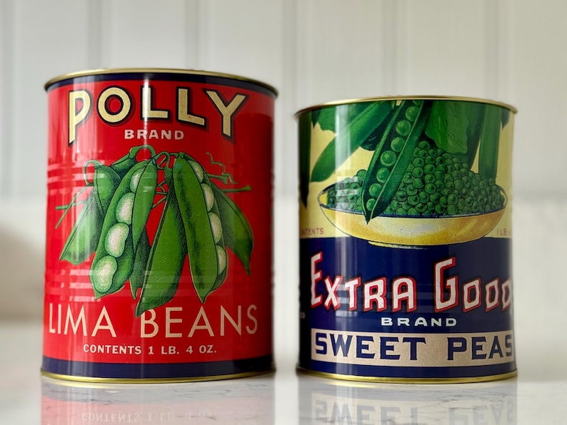 May include: Two vintage-style cans of vegetables. One is red with "POLLY BRAND LIMA BEANS" and a graphic of lima beans. The other is green and blue with "EXTRA GOOD BRAND SWEET PEAS" and a pea pod graphic. Each can is 1 lb 4 oz.