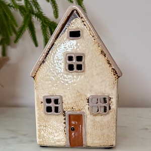 Peut inclure: Une figurine de maison en c&eacute;ramique avec un ext&eacute;rieur cr&egrave;me et un toit marron. La maison a quatre fen&ecirc;tres carr&eacute;es et une porte marron. La figurine est un objet d&eacute;coratif.