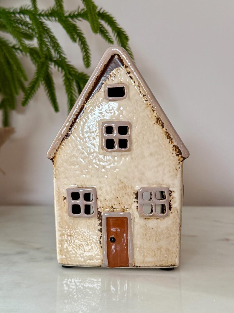 Peut inclure: Une figurine de maison en c&eacute;ramique avec un ext&eacute;rieur cr&egrave;me et un toit marron. La maison a quatre fen&ecirc;tres carr&eacute;es et une porte marron. La figurine est un objet d&eacute;coratif.