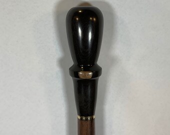 May include: A dark brown wooden walking stick with a decorative top. The top is a rounded, bulbous shape with a gold band around the middle. The stick is smooth and polished.