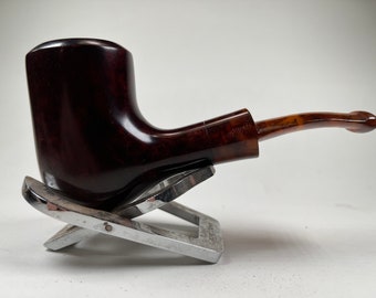 May include: A dark brown wooden pipe with a brown amber stem, resting on a silver stand.