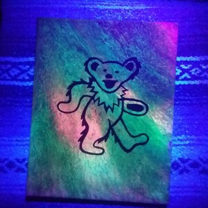 May include: A black and white silhouette of a dancing bear on a green, pink, and blue canvas. The canvas is painted with a swirling, abstract design.