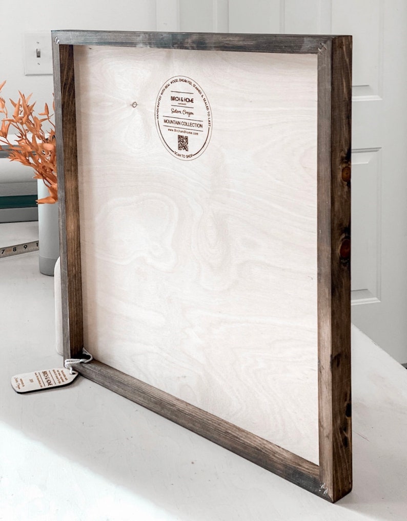 Puede incluir: Un letrero de madera con un marco marr&oacute;n oscuro. El letrero est&aacute; en blanco y listo para ser personalizado. La parte posterior del letrero tiene una peque&ntilde;a pegatina redonda con el texto "Birch & Home, Salem, Oregon, Mountain Collection, www.birchandhome.com, Scan to Shop".