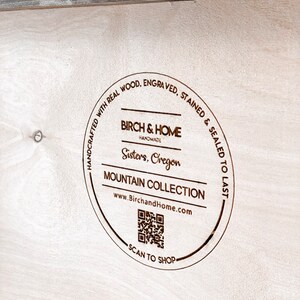Puede incluir: Un letrero redondo de madera con el texto "HANDCRAFTED WITH REAL WOOD. ENGRAVED. STAINED & SEALED TO LAST" que rodea un logotipo que dice "BIRCH & HOME HANDMADE Sisters, Oregon MOUNTAIN COLLECTION www.BirchandHome.com" con un c&oacute;digo QR y el texto "SCAN TO SHOP".