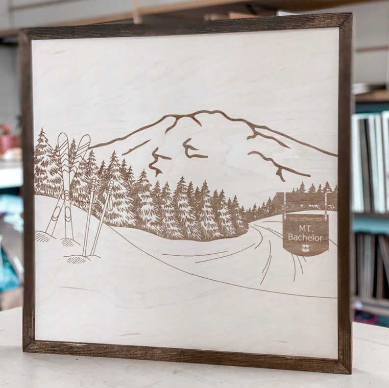 Puede incluir: Un letrero de madera con un dise&ntilde;o grabado con l&aacute;ser de una cordillera, pistas de esqu&iacute; y dos pares de esqu&iacute;s. El letrero tambi&eacute;n incluye el texto "The Crest to MT. Bachelor".
