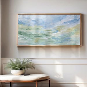 May include: A rectangular landscape painting in a gold frame featuring abstract brushstrokes in shades of light blue, sage green, and cream. The artwork displays a horizontal composition with blended colors that evoke a soft, atmospheric sky and landscape.