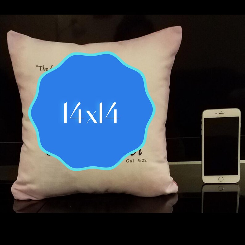 Puede incluir: Una almohada blanca con un c&iacute;rculo azul en el centro. El c&iacute;rculo tiene el texto "14x14" en blanco. La almohada tiene el texto "El fruto del Esp&iacute;ritu es..." y "Gal. 5:22" impreso en ella.