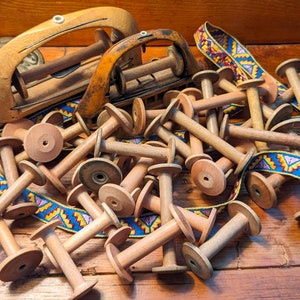 May include: A pile of wooden spools with a colorful ribbon woven through them. The spools are various sizes and shapes, and some have a small hole in the center. The ribbon is a mix of red, blue, yellow, and white.