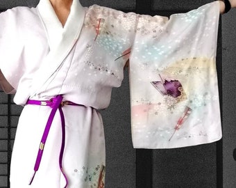 May include: A white silk kimono with a purple sash and a colorful floral pattern. The kimono has a traditional Japanese design with a wide collar and long sleeves.