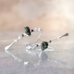 May include: A pair of silver wire earrings featuring green and white stones. The earrings are dangling and have a delicate, minimalist design.