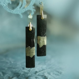 May include: A pair of black rectangular earrings with gold accents. The earrings are hanging from a gold hook.