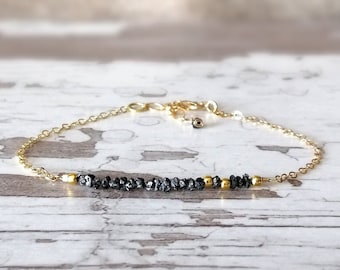 May include: A delicate gold chain bracelet with a row of black diamond beads and gold beads.