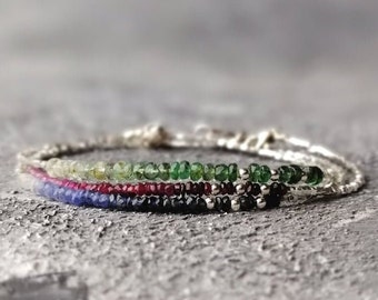 May include: A silver bracelet with four rows of gemstone beads. The top row is green, the second row is red, the third row is blue, and the bottom row is silver.