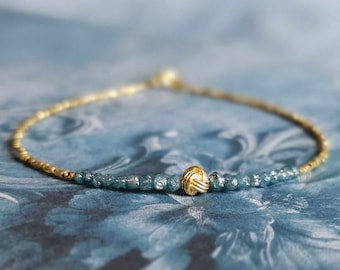 May include: A delicate gold bracelet with a knot charm and blue gemstone beads.