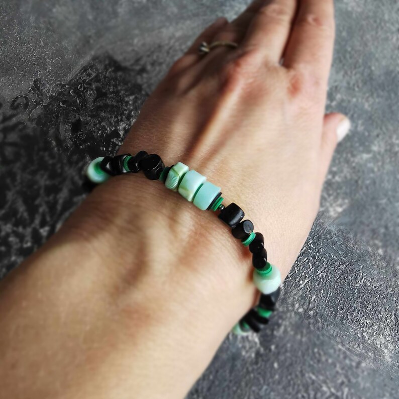 May include: A black and green beaded bracelet with a light blue and green stone accent.