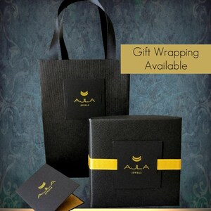 May include: Black gift boxes with a gold ribbon and a gold logo that says "Ajla Jewelz". The boxes are on a black and white striped bag with the same logo. The text "Gift Wrapping Available" is in a yellow box.