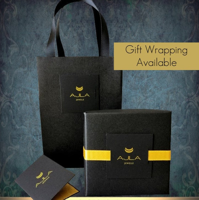 May include: Black gift boxes with a gold ribbon and a gold logo that says "Ajla Jewelz". The boxes are on a black and white striped bag with the same logo. The text "Gift Wrapping Available" is in a yellow box.
